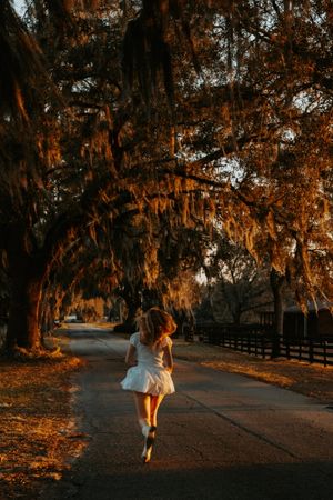 Person in white dress walking along a tree-lined path during sunset.