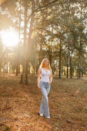 A casual outdoor portrait in a sunlit forest with light streaming through pine trees.