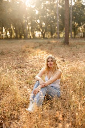 Dreamy sunset portrait in tall grass with soft golden light filtering through forest trees in background.