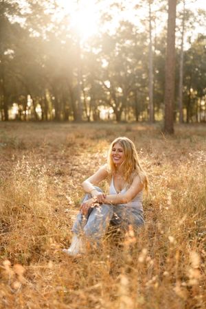 Person sitting in golden field at sunset with tall trees in background creating dreamy atmosphere.