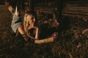 Person lying in field of wildflowers at sunset near wooden fence.