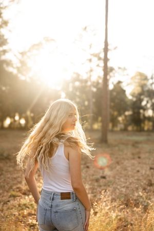 Woman in denim and white top enjoying golden hour in natural setting.