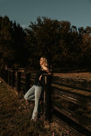 Moody autumn photoshoot by a rustic wooden fence with wildflowers in the foreground.