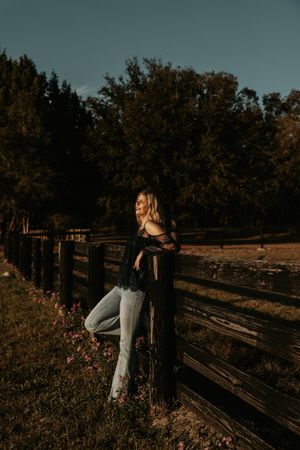 Woman leaning on rustic wooden fence during moody sunset.