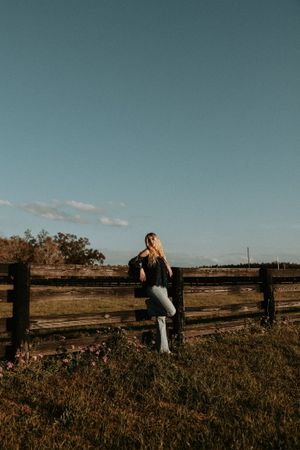Figure walking through tall grass near wooden fence during late afternoon light.