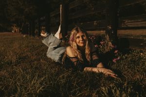 Woman relaxing on wooden fence in rustic countryside setting.
