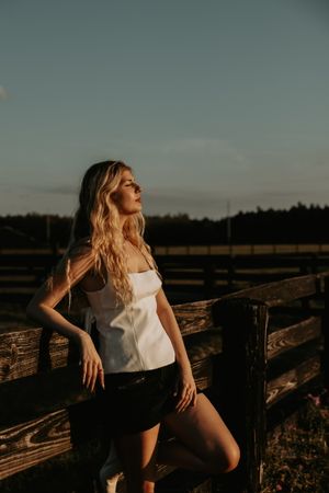 Artistic sunset photoshoot featuring a person in white top and shorts posing against rustic wooden fencing.