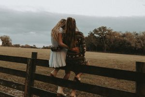 Two people sitting together on wooden fence at countryside farm during sunset.