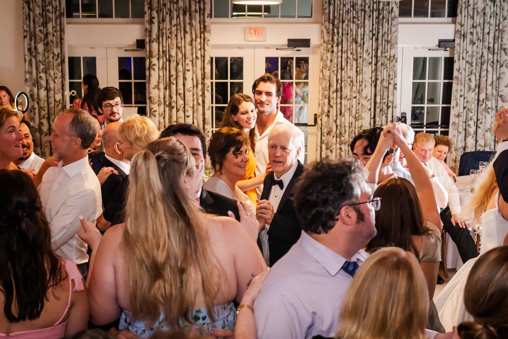 Wedding guests dance and celebrate together on a crowded dance floor during an indoor reception.