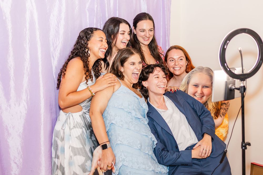 A group of people pose and laugh together in front of a purple backdrop during a photo booth session.