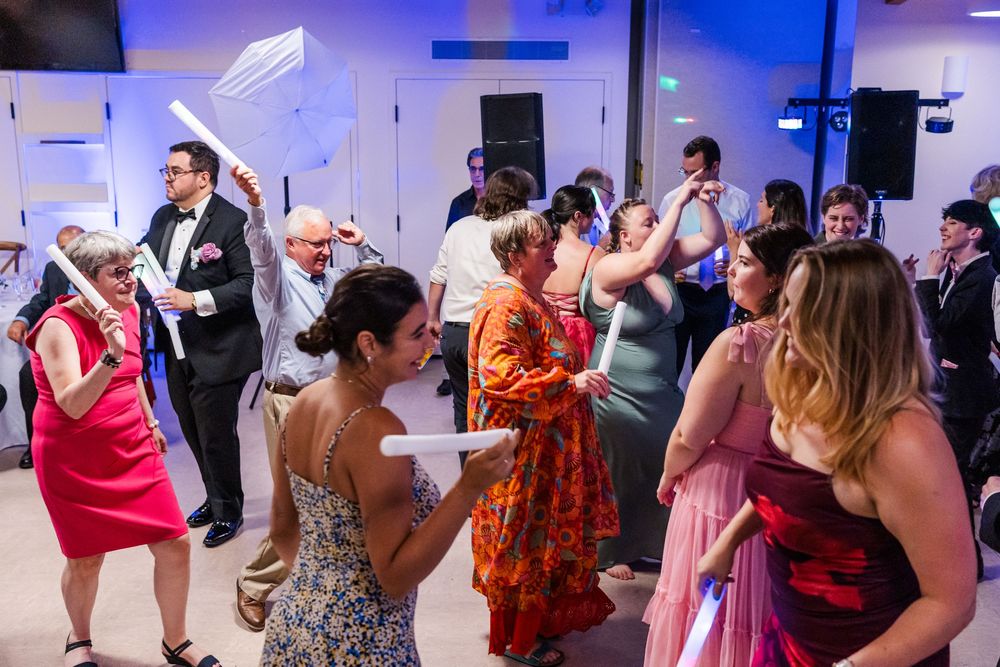 Wedding guests dance and celebrate on a dance floor illuminated with blue lighting at an indoor reception.