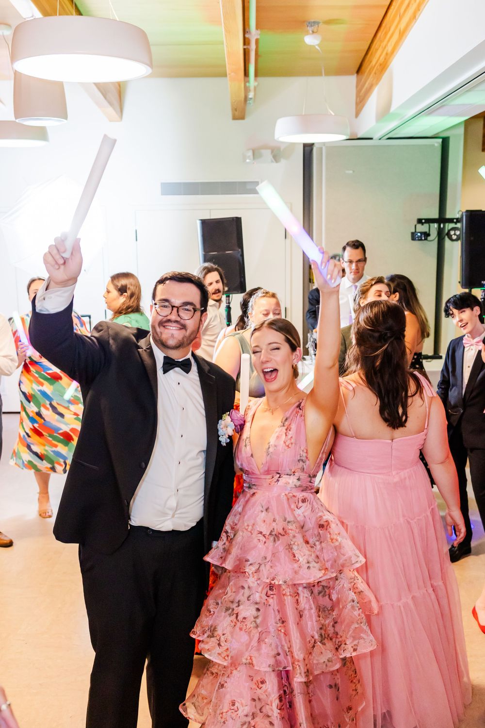 Wedding guests dancing and celebrating joyfully at a reception with pink and floral attire.