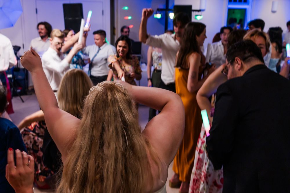 Energetic crowd dancing with raised arms at a lively indoor party with blue lighting.