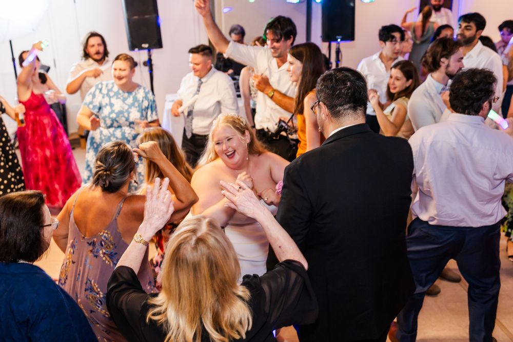 Wedding guests dance and celebrate together on a lively dance floor during an evening reception celebration.