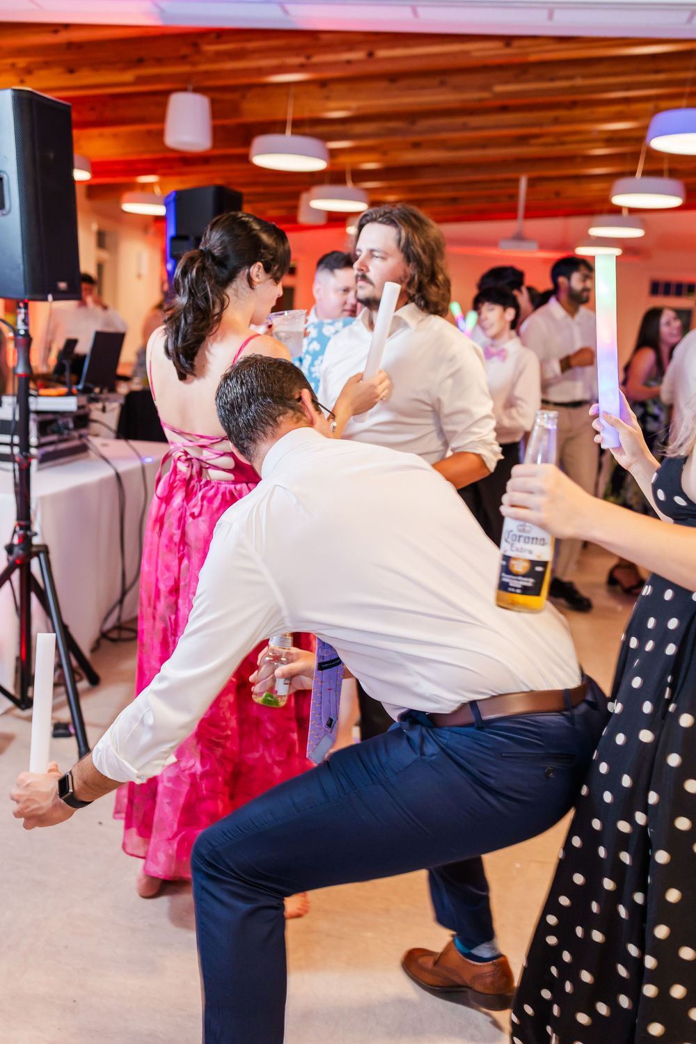 Wedding guests dance energetically in a reception hall with polka dot dresses and white shirts visible.