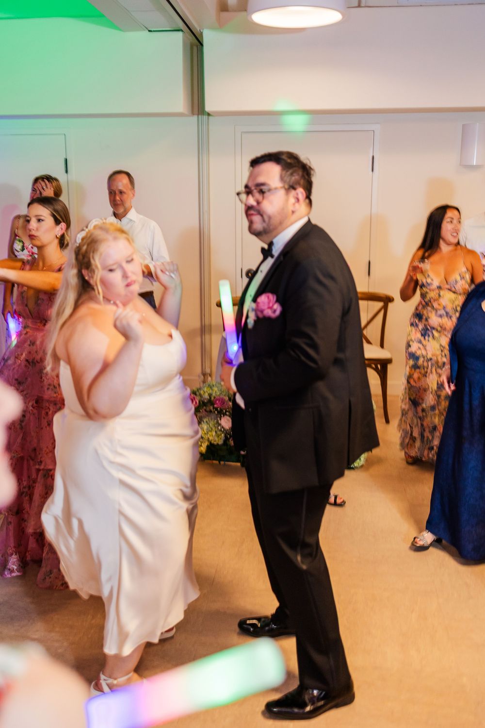Wedding party members dancing in formal attire during a reception with green lighting.