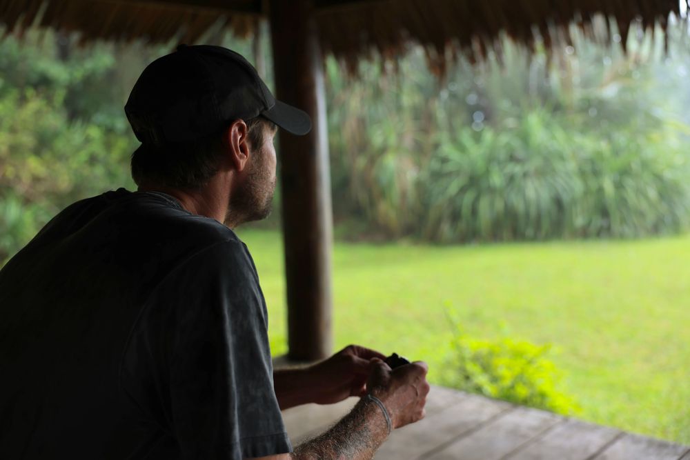 Silhouette of person relaxing under a thatched roof hut overlooking tropical landscape.
