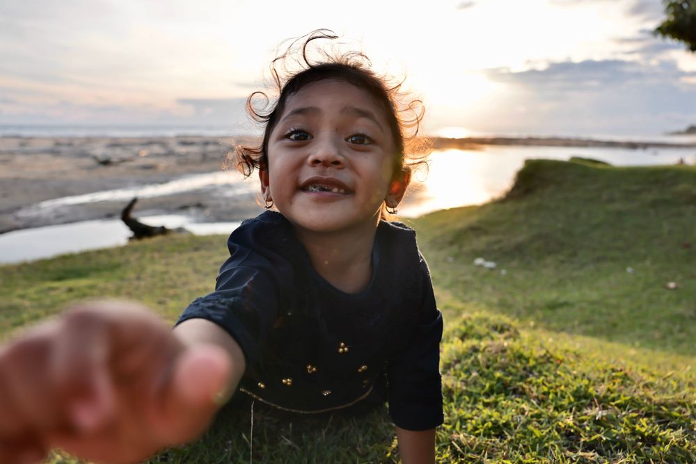 Children playing outdoors at sunset near a grassy coastal area.