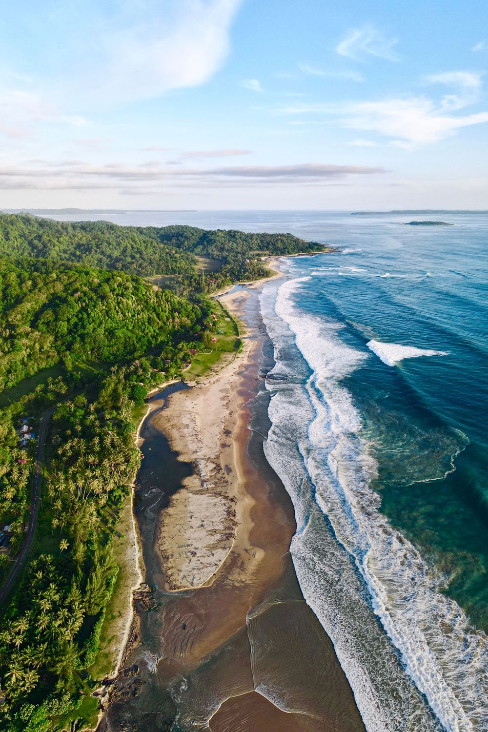Stunning aerial view of a tropical coastline with turquoise waves crashing on a curved beach.