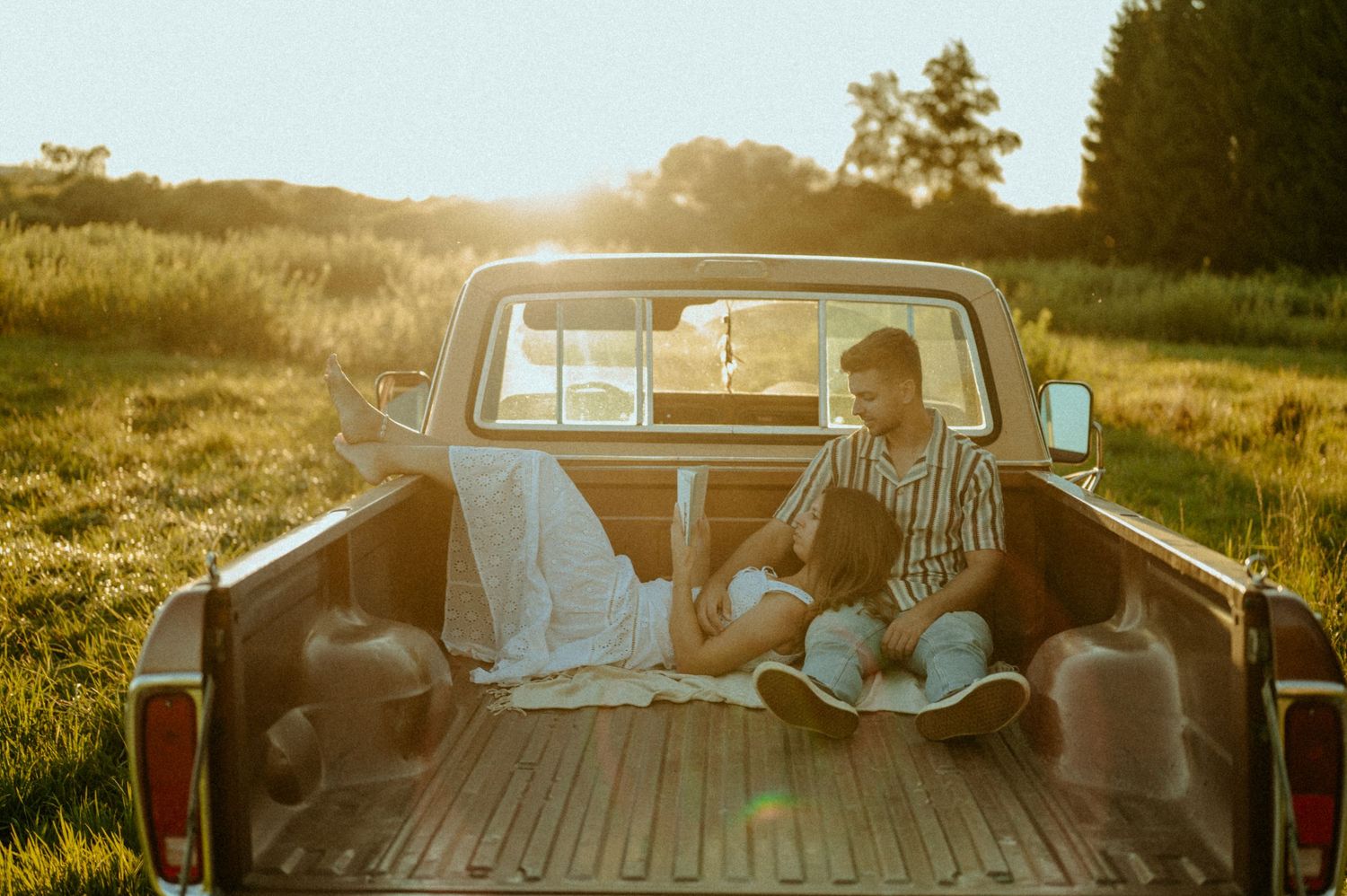 Vintage pickup truck parked in a golden field during sunset with people sitting in the back.