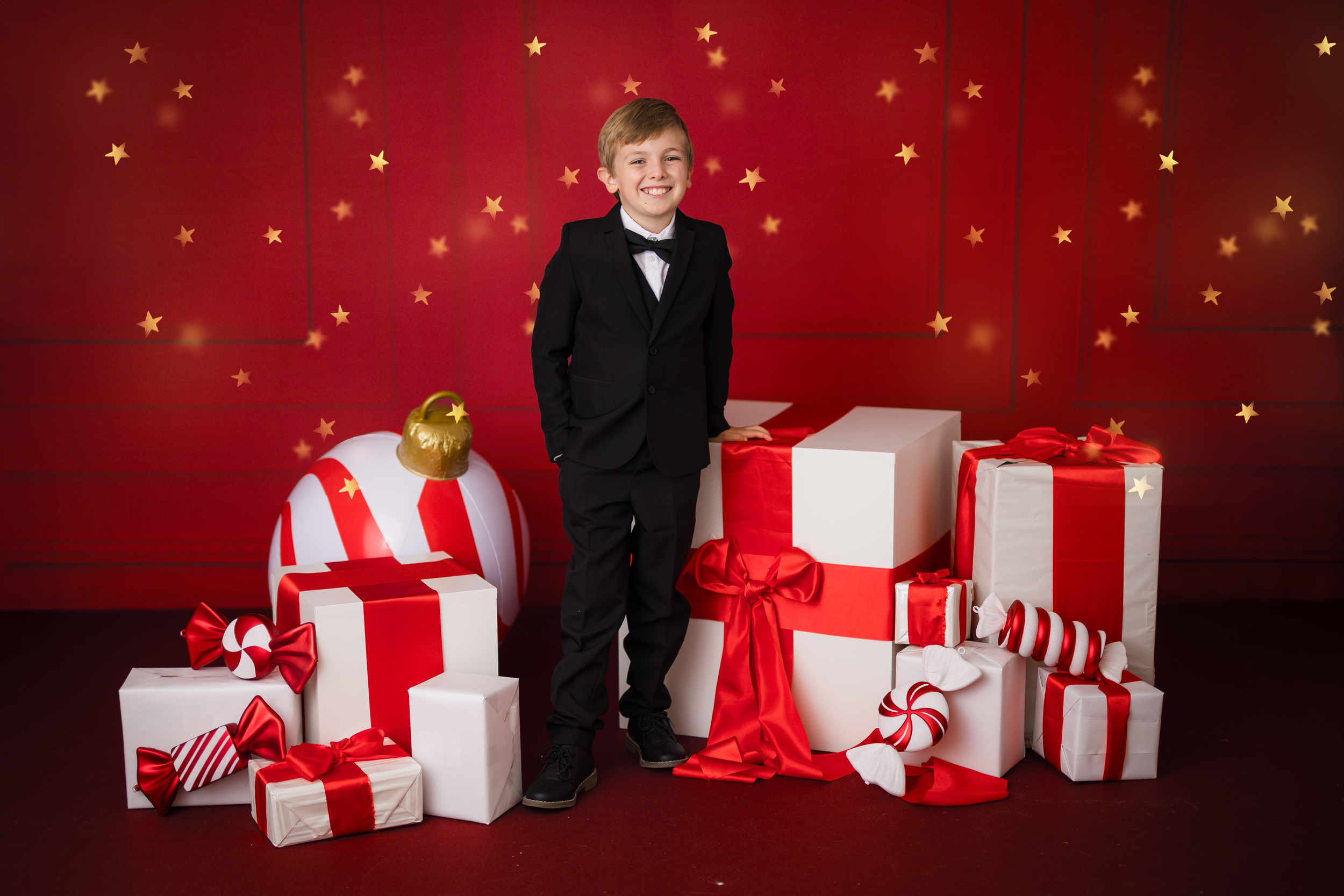 Holiday themed photo session with presents and festive red and white decor against sparkly backdrop.