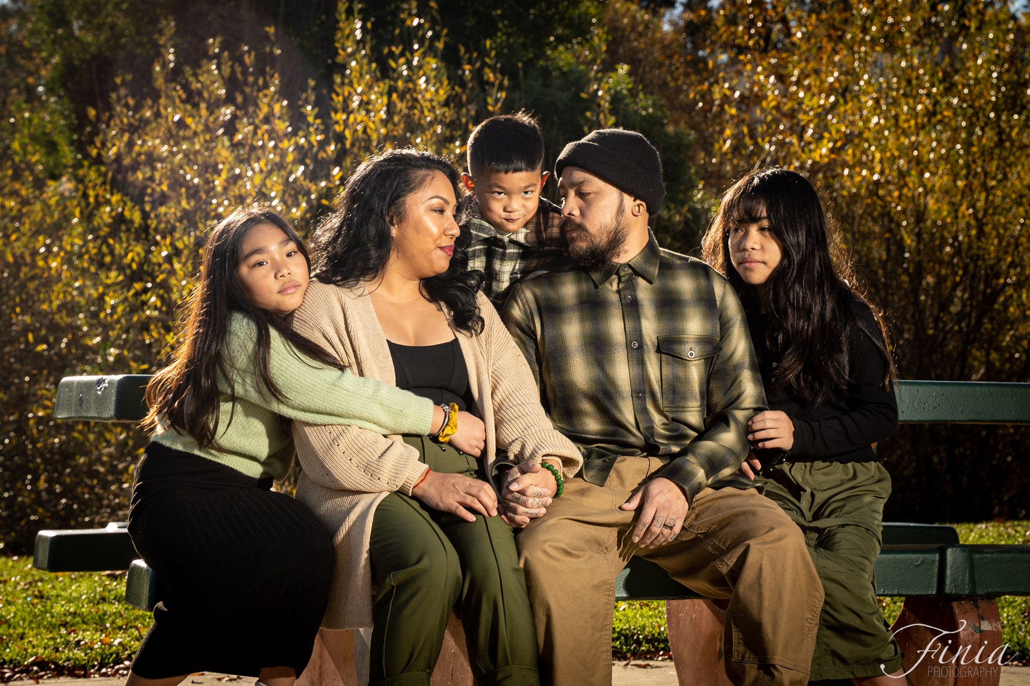 A group sits together on a wooden bench sharing laughter during a golden autumn afternoon photo session.