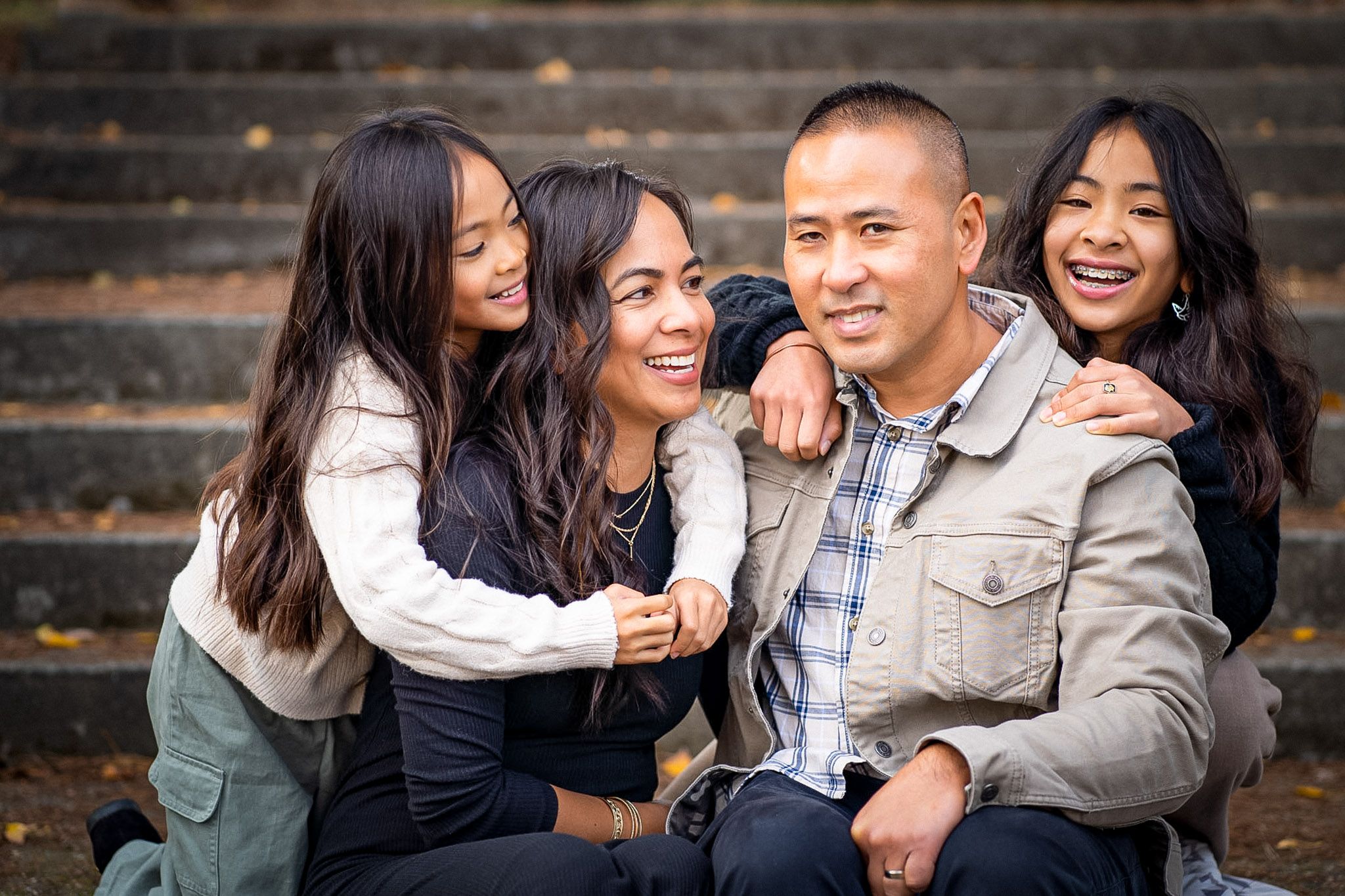 A family laughs together while sitting on outdoor wooden steps during a casual photo session.