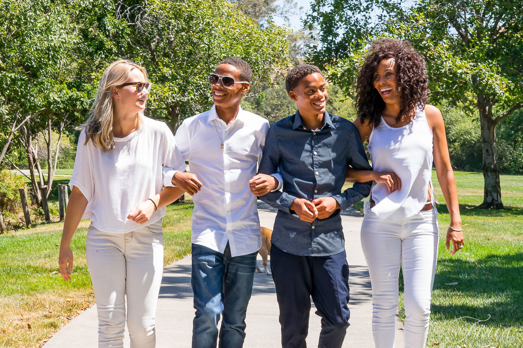 A group of friends walking together outdoors in white and navy outfits on a sunny summer day in a park setting.