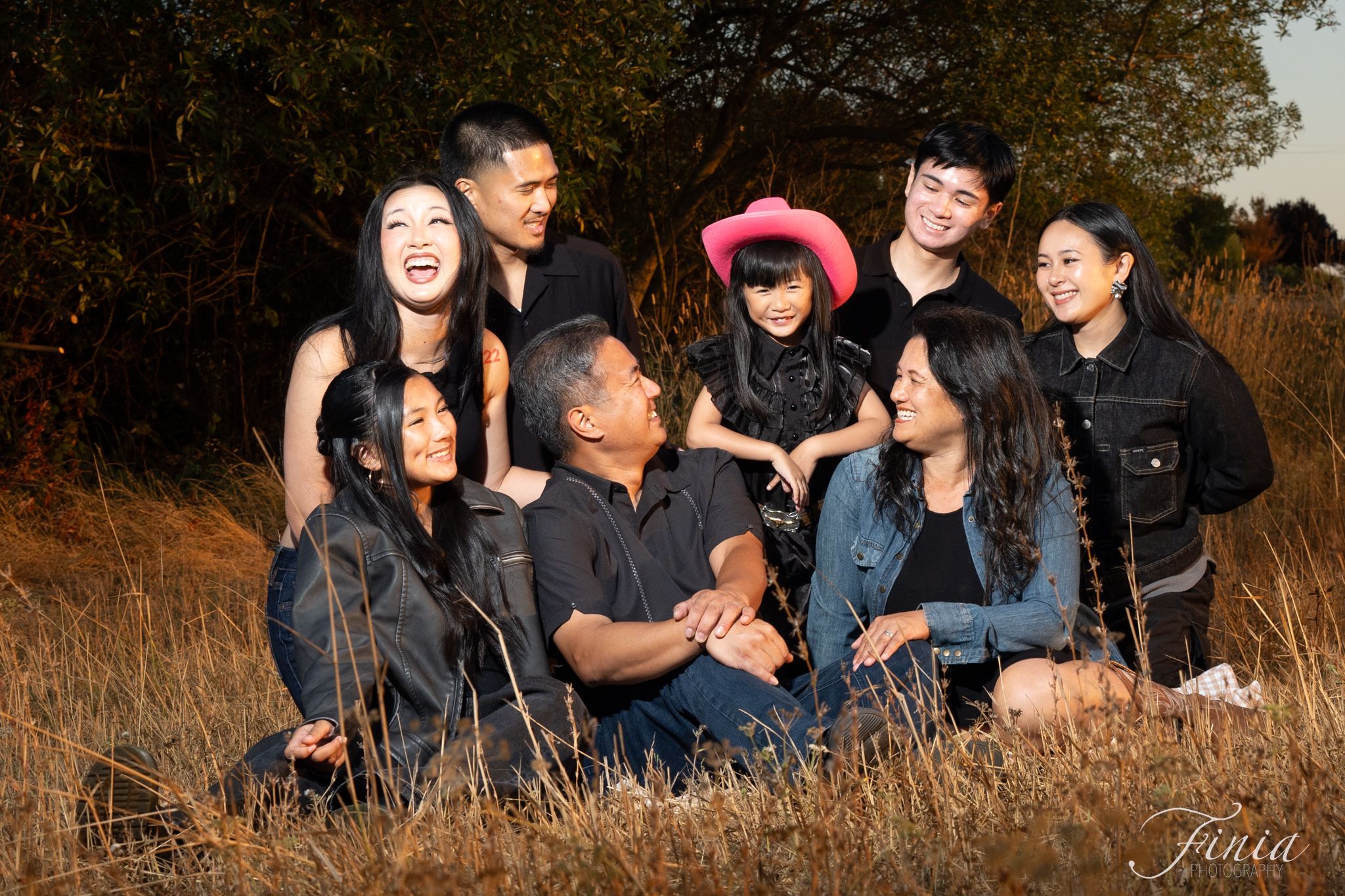 A group of people pose playfully in tall grass during a casual outdoor photo session at golden hour.