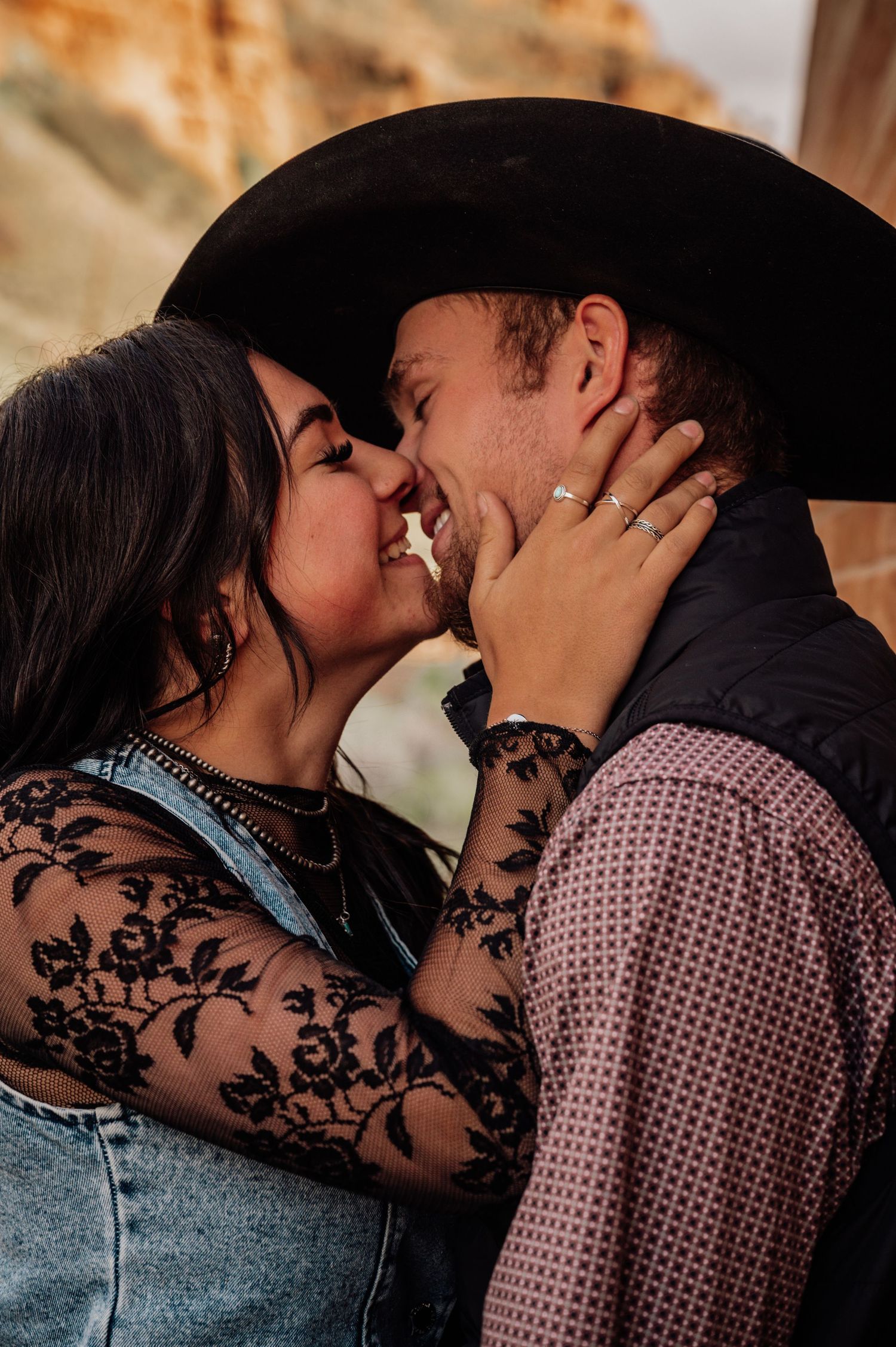 Romantic couple in western attire sharing intimate moment under brim of cowboy hat.