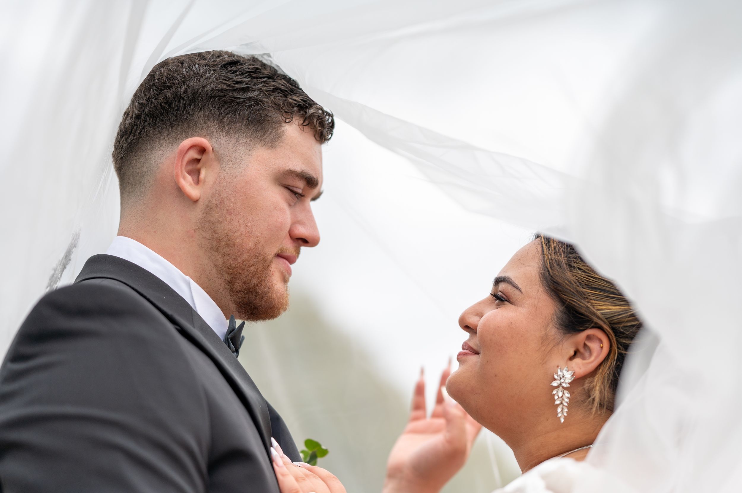 Un couple romantique partage des moments intimes lors de leur célébration de mariage sous un drapé en tissu blanc.