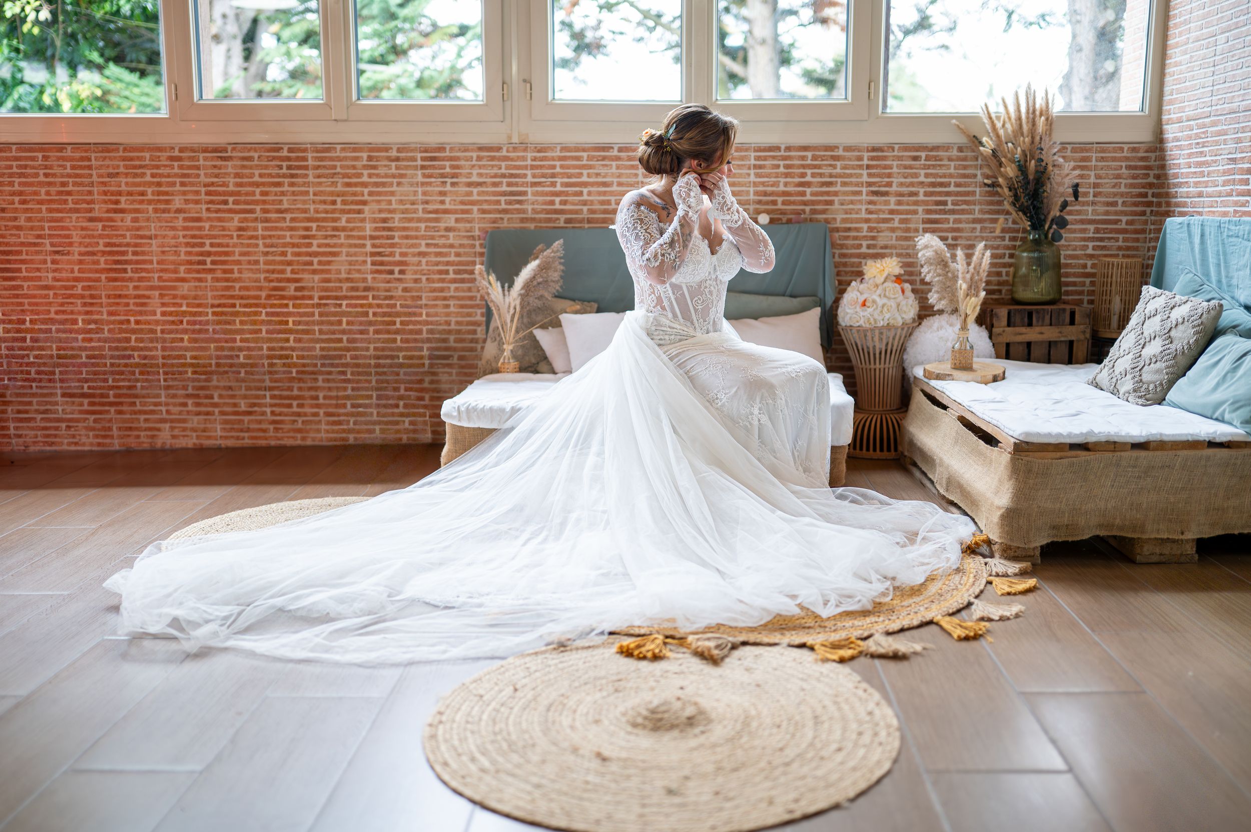 Une robe de mariée blanche fluide avec un train dramatique s'étend sur un plancher de bois franc poli dans une pièce ensoleillée.