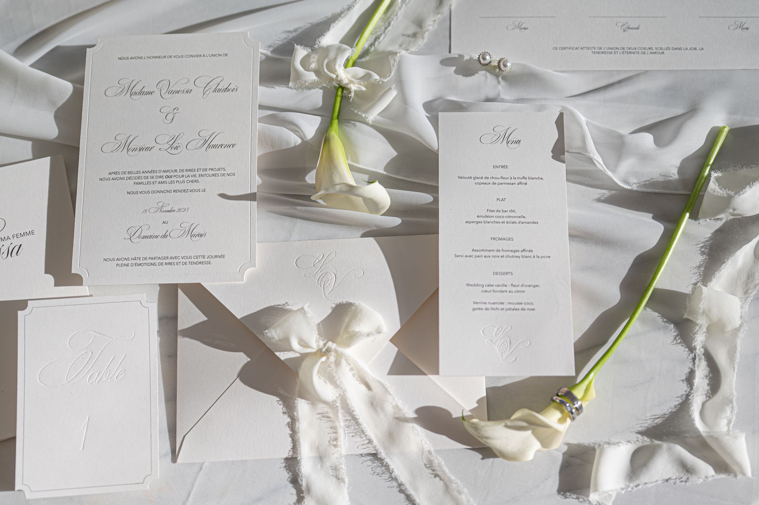 Invitations de mariage en papier blanc disposées dans un motif de grille avec des fleurs de lys calla éparpillées partout en flatlay.