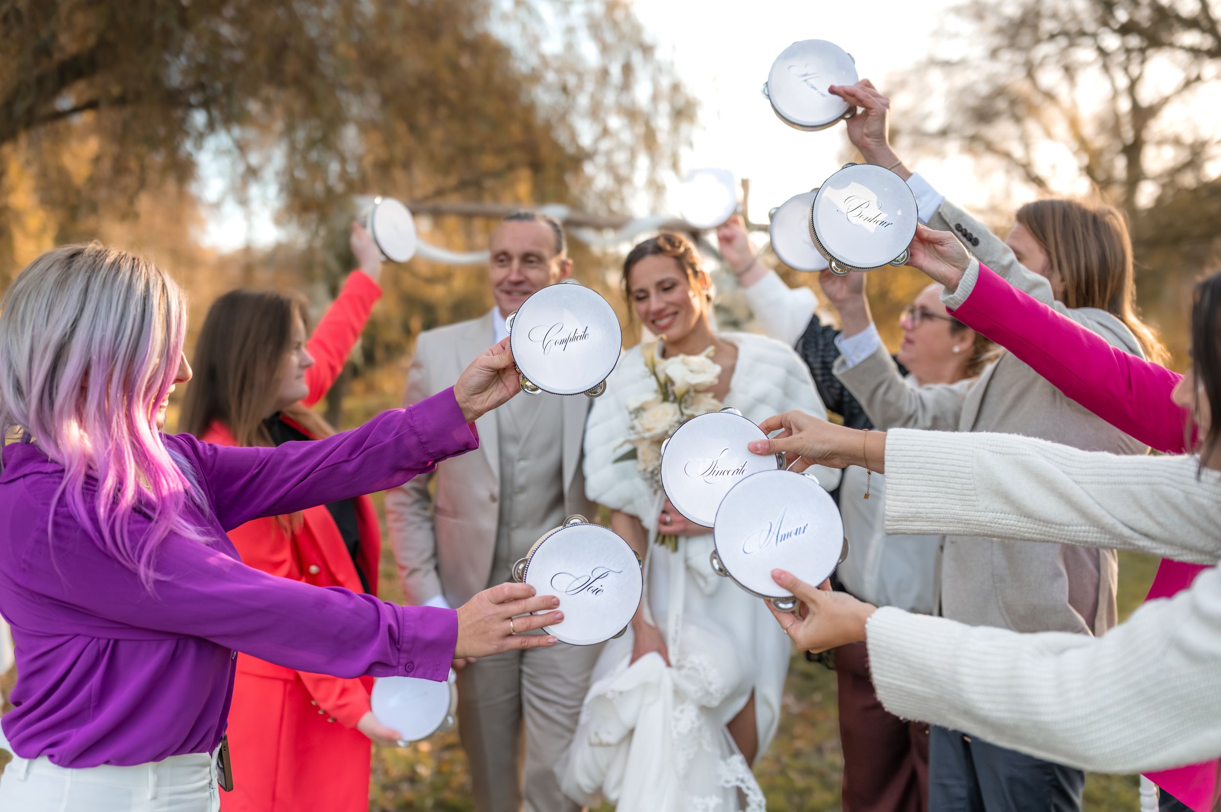 Un groupe d'invités au mariage célèbre en tenant des assiettes en papier blanc dans un moment ludique en plein air au coucher du soleil.