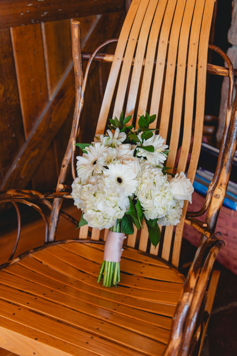 White floral bouquets arranged in a row on wooden slat chairs at a wedding venue.