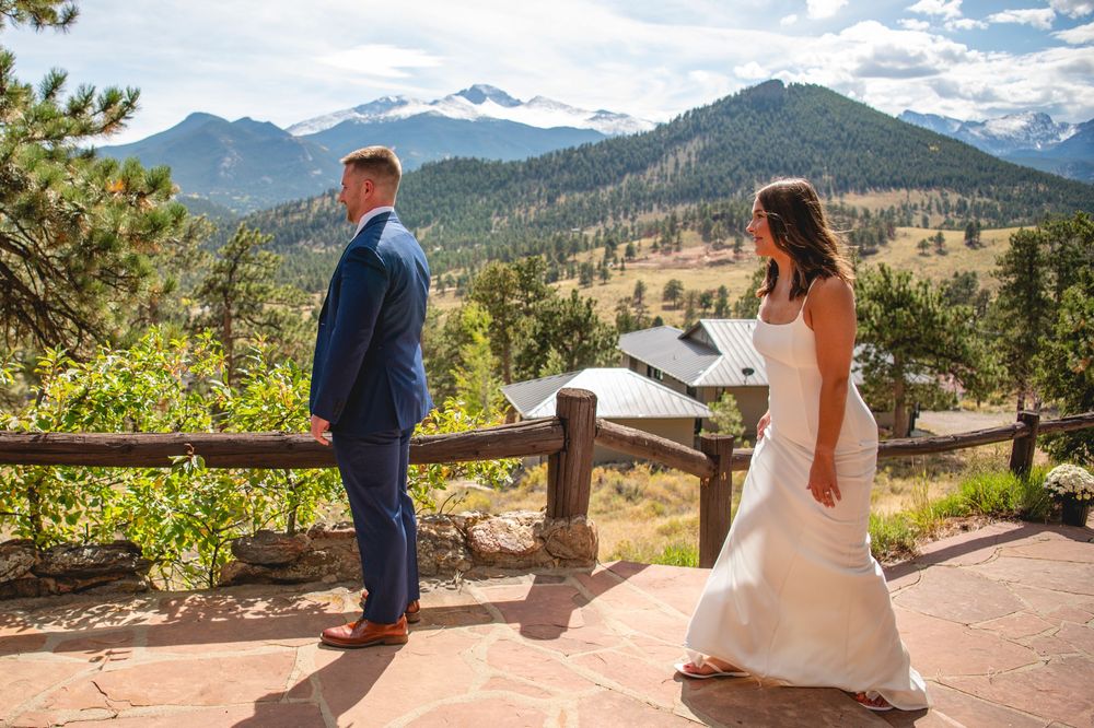 Wedding couple stands on scenic mountain overlook with dramatic Rocky Mountain peaks and forest views.