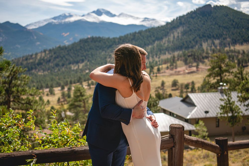 Two people embrace while looking out at scenic mountain views from a wooden deck in Colorado.