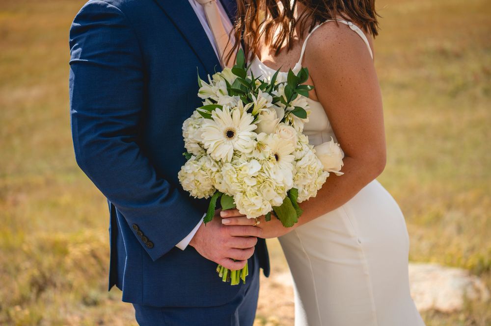 A couple in wedding attire holds hands during golden hour in a rustic outdoor setting.