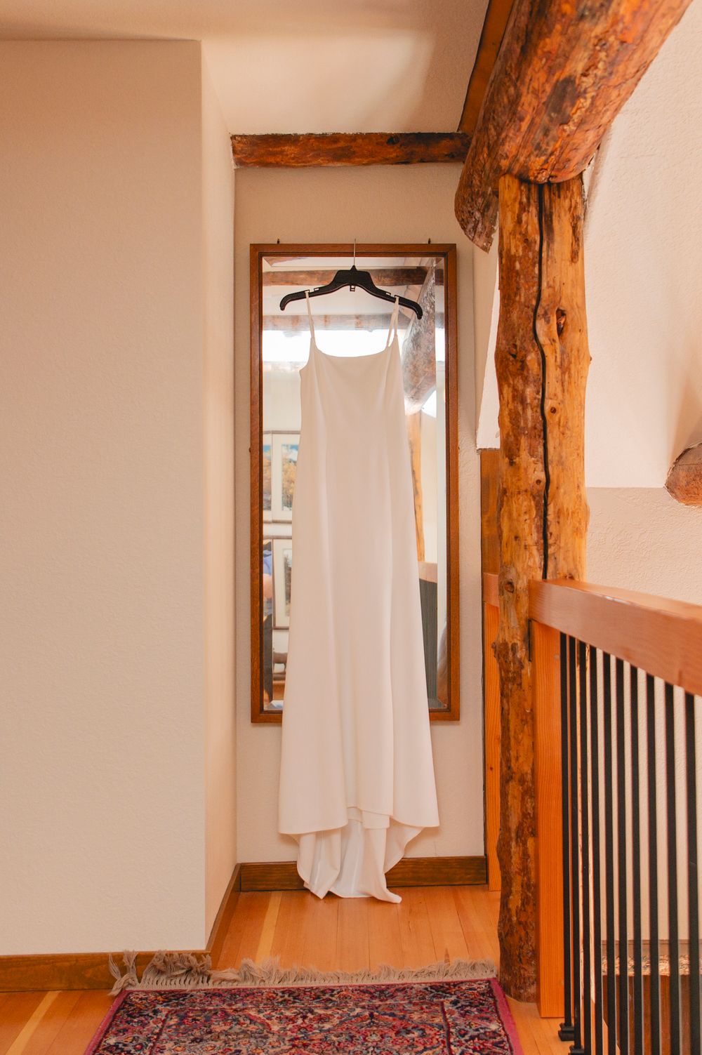 White dress hanging in rustic hallway with exposed wooden beams and oriental rug on hardwood floor.
