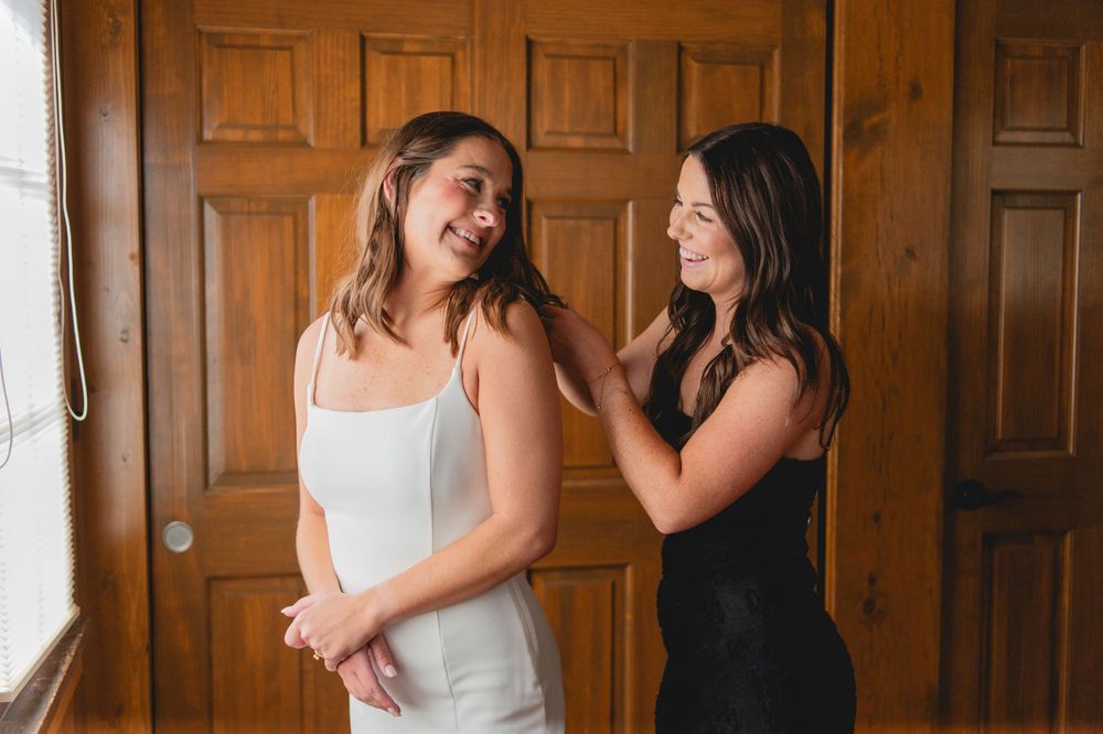 Two people share joyful moments together in front of wooden paneled walls during a wedding preparation.