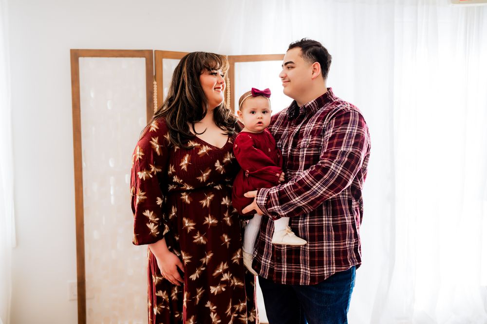 A couple in matching burgundy plaid outfits share romantic moments in a bright indoor setting during a photo session.