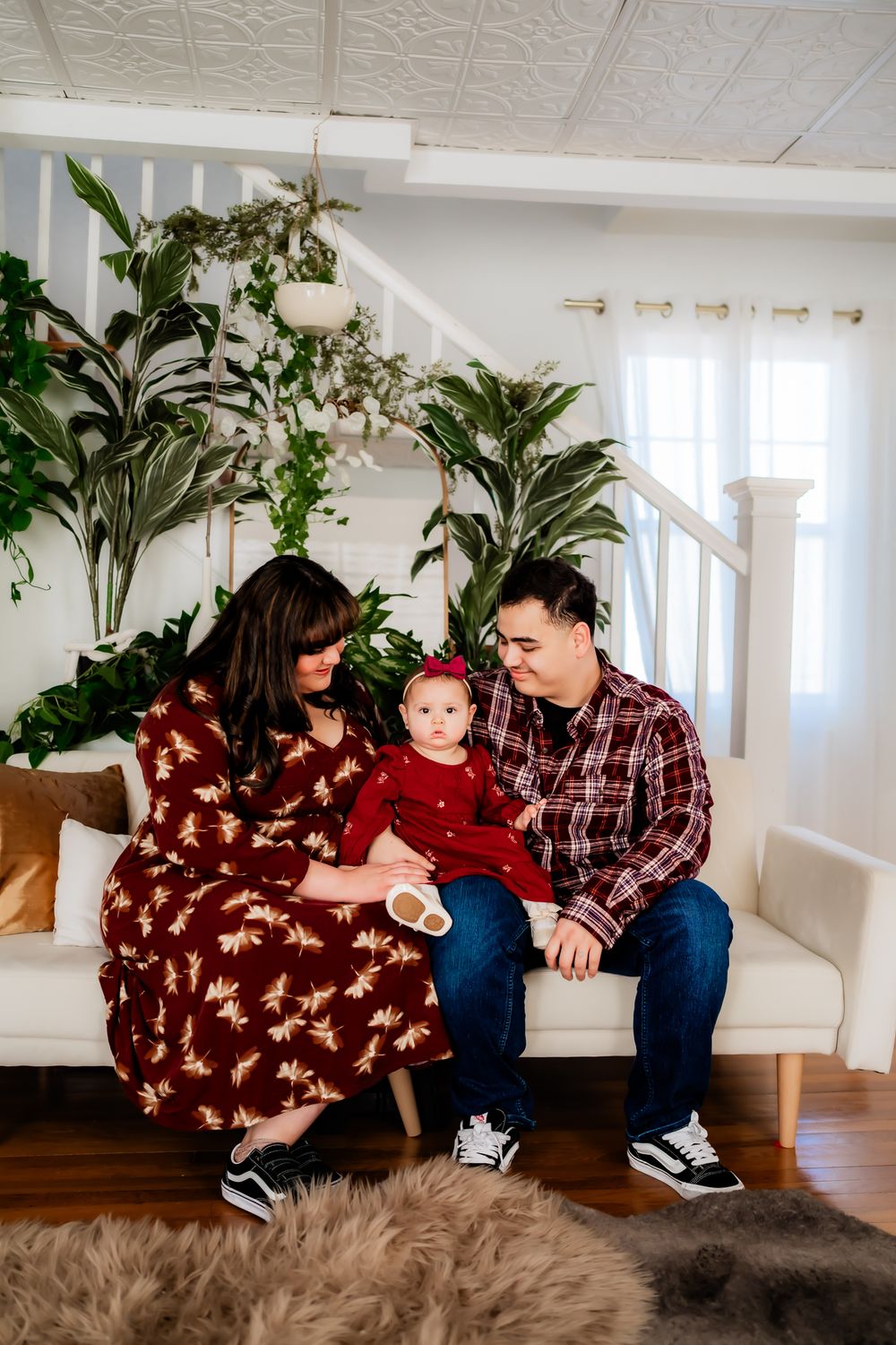 A family shares tender moments together while sitting on a white bench in a bright room with plants.