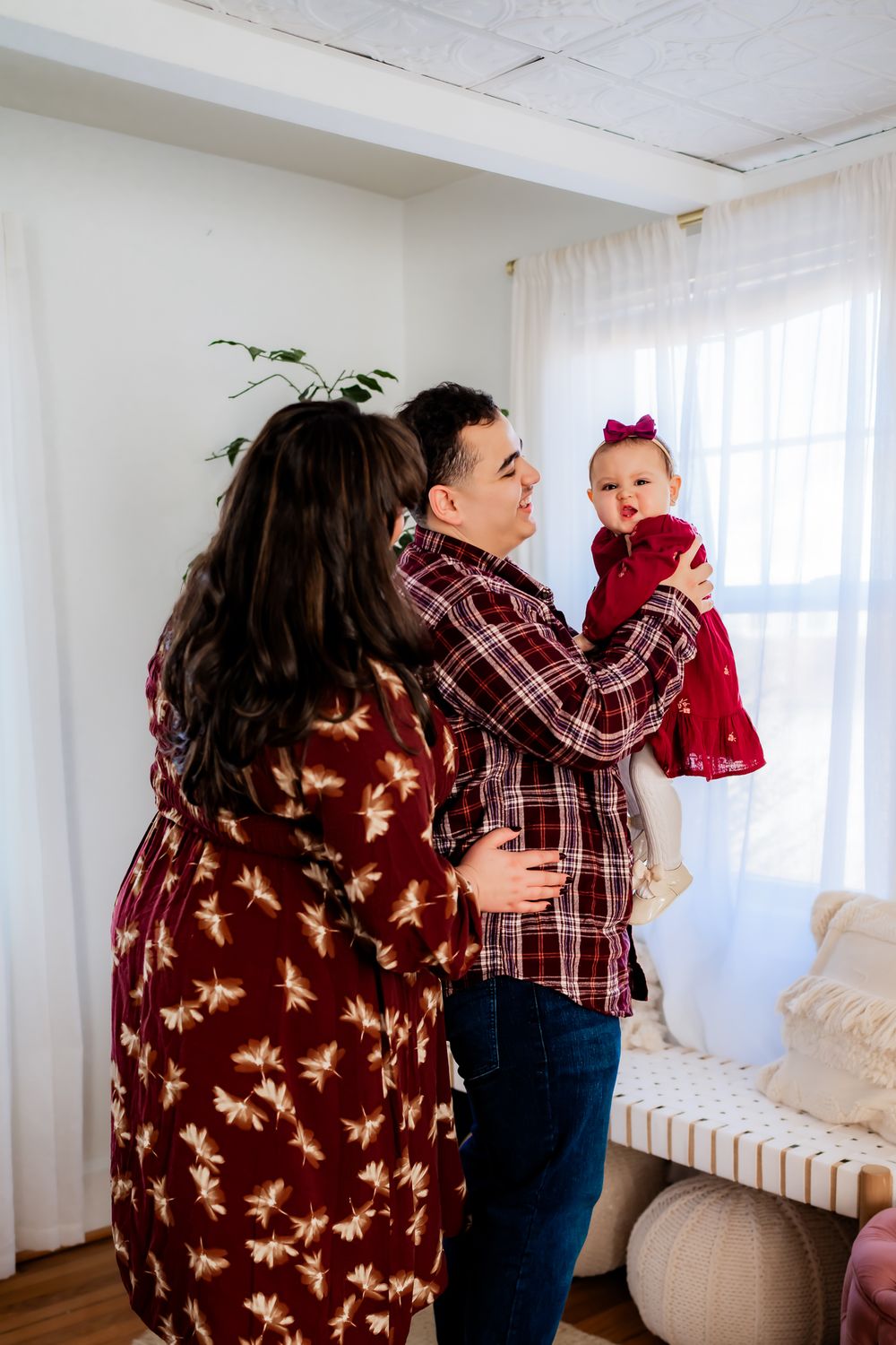 A family embraces while sitting together in a sunlit room with white walls and flowing curtains.