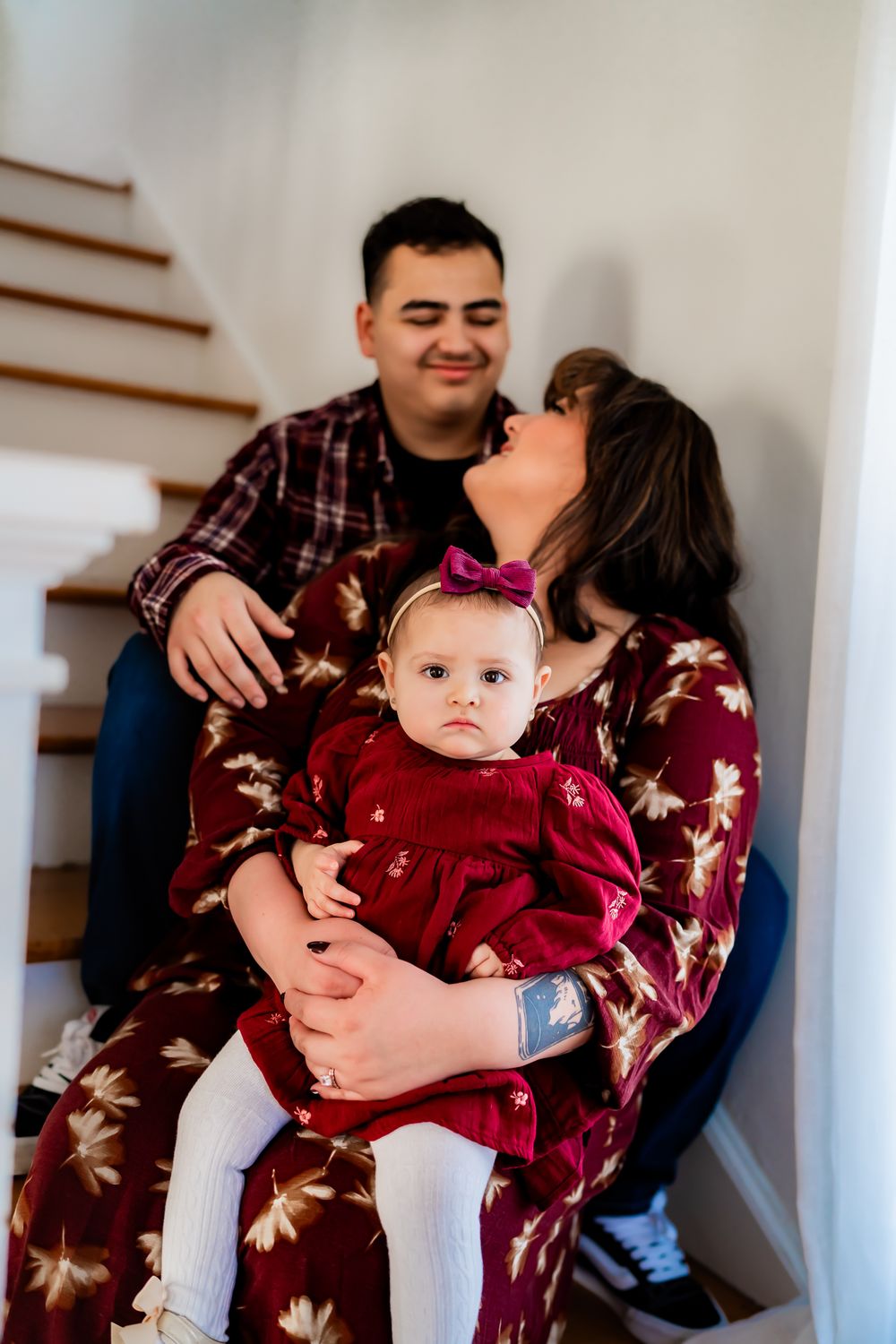 Family wearing matching burgundy outfits poses on white staircase for holiday photos.