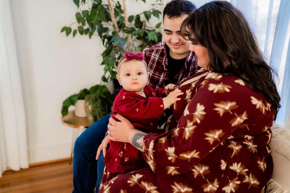 Family members wearing cozy winter sweaters share joyful moments in a sunlit room with plants.