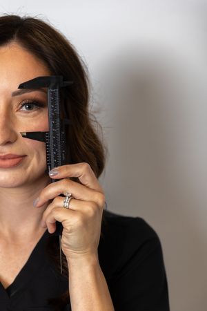 A person wearing black holds a measuring device against their face in a sequence of similar poses against a gray background.