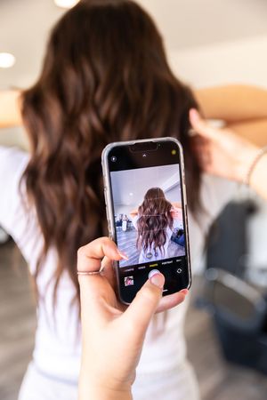 A series of smartphone photos showing someone taking selfies of their long brown wavy hair from behind.