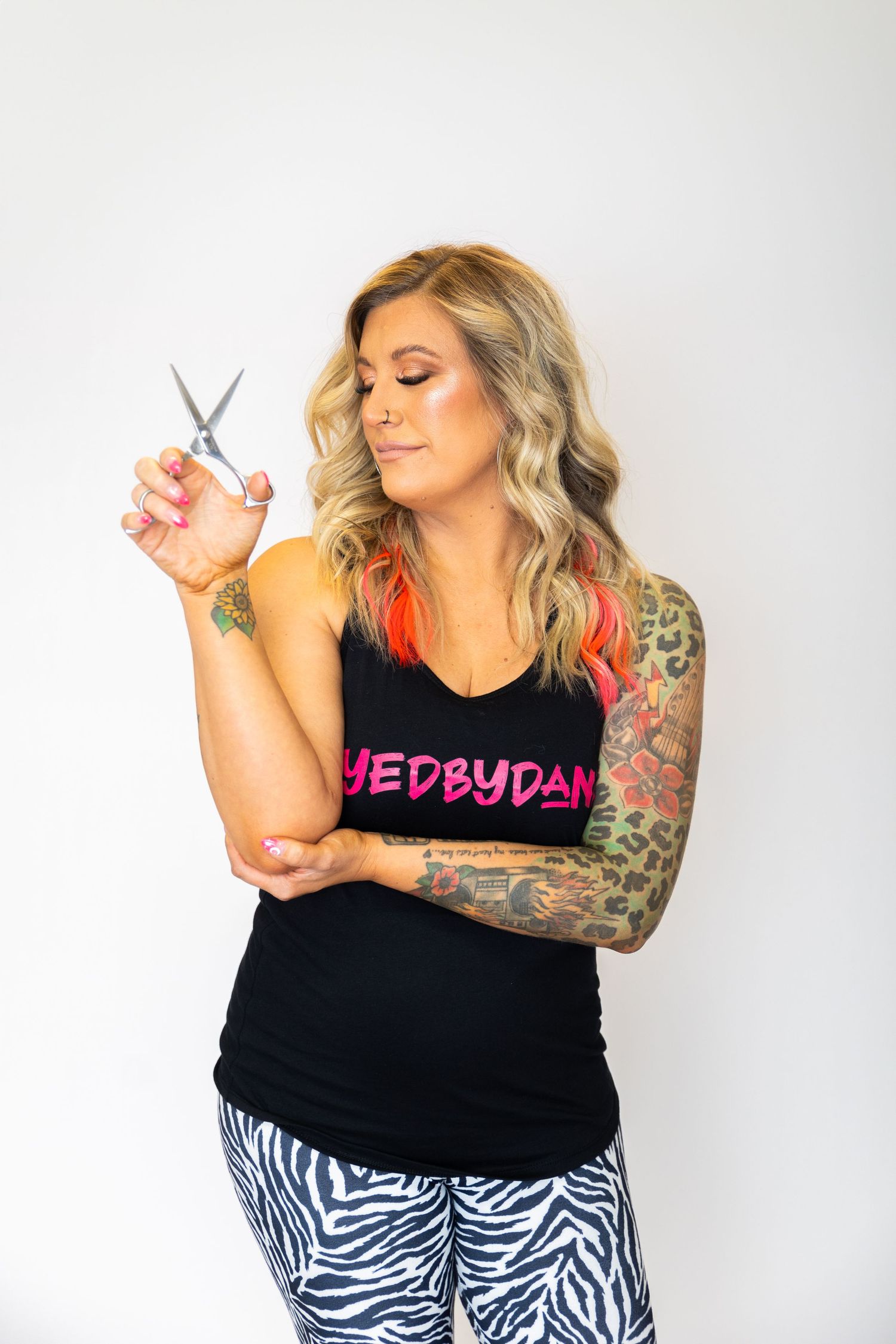 Woman in black tank top with pink text and tattoos poses in front of white background.