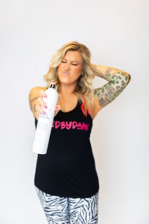 Woman in black tank top and zebra print pants poses with white water bottle against white background.