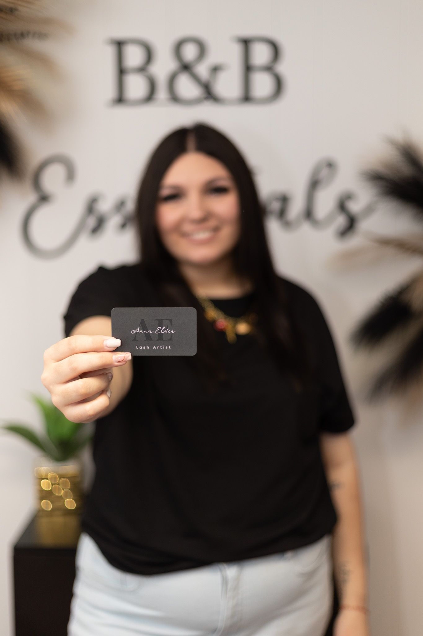 Someone in a black shirt holding a business card against a white wall with B&B signage in the background.